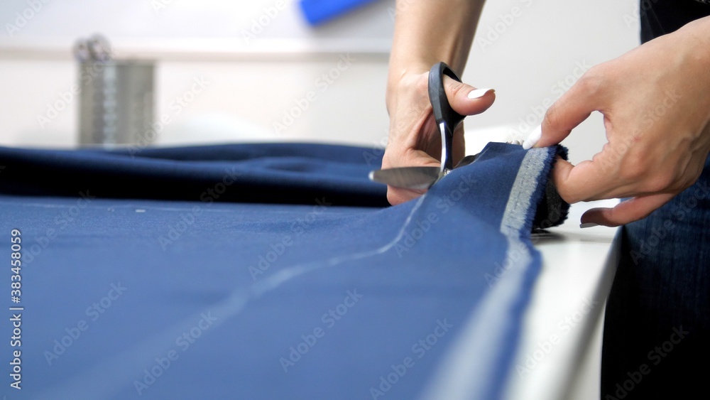 Female hands cut the fabric with scissors, close-up. Female tailor in a sewing workshop. Sewing workshop work. Repair and sewing of clothes. Atelier workers 