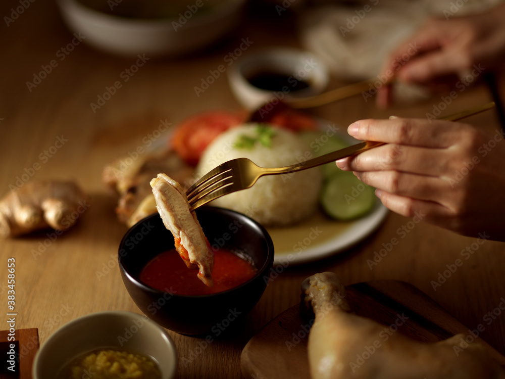 Woman eating Hainanese chicken rice, dipping chicken in the chilli sauce Woman eating Hainanese chicken rice, dipping chicken in the chilli sauce