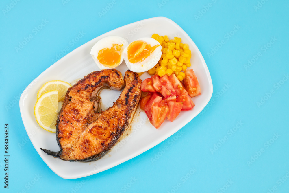 fried salmon with boiled egg, tomato and corn on white dish
