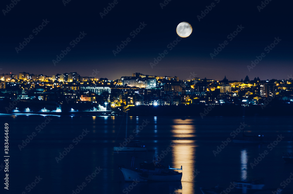 Night view of Cascais, Portugal with full moon reflecting on water and fishing boats Night view of Cascais, Portugal with full moon reflecting on water and fishing boats