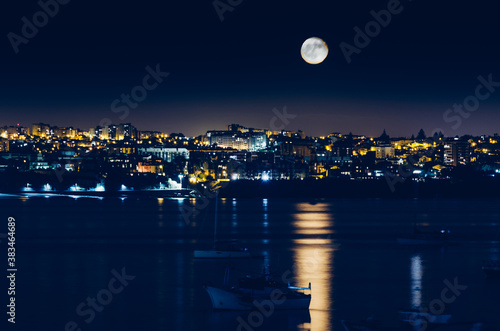 Night view of Cascais, Portugal with full moon reflecting on water and fishing boats
