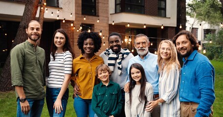 Portrait of mixed-races happy family at dinner outdoor in yard smiling and posing to camera on weekend spending together. Multi ethnic people at barbeque. Celebration. Parents and kids. Generations.