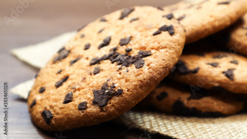 American chocolate chip cookies on a brown wooden table and on a linen napkin close-up. Traditional rounded crunchy dough with chocolate chips. Bakery. Delicious dessert, pastries. Rural still life.