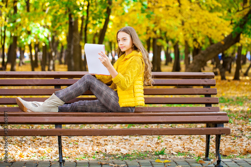 Young girl draws with a pencil in the sketchbook, autumn park outdoor