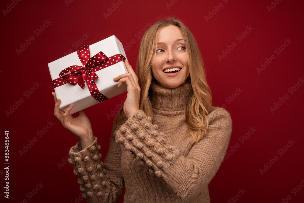 Charming blonde woman holding gift with red ribbon. Studio shot red background. New Year Birthday Holiday concept Charming blonde woman holding gift with red ribbon. Studio shot red background. New Year Birthday Holiday concept