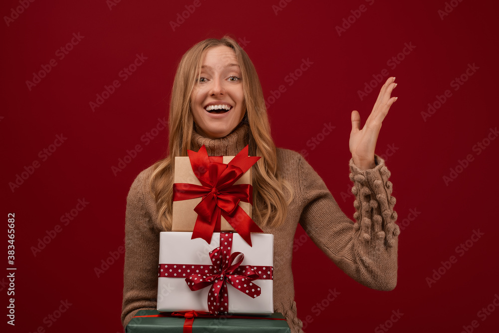 Charming young blonde woman holds a lot of gift boxes. Studio shot red background. New Year Birthday Holiday concept Charming young blonde woman holds a lot of gift boxes. Studio shot red background. New Year Birthday Holiday concept