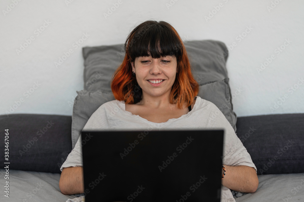 Alternative young woman lying on the bed while checking her tablet with a surprised face in a warm home environment Alternative young woman lying on the bed while checking her tablet with a surprised face in a warm home environment