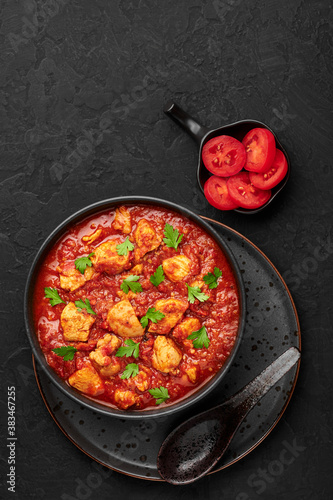 Chicken Madras Curry in black bowl on dark slate table top. Indian cuisine dish with with chicken meat and spicy masala gravy. Asian food and meal. Top view. Copy space