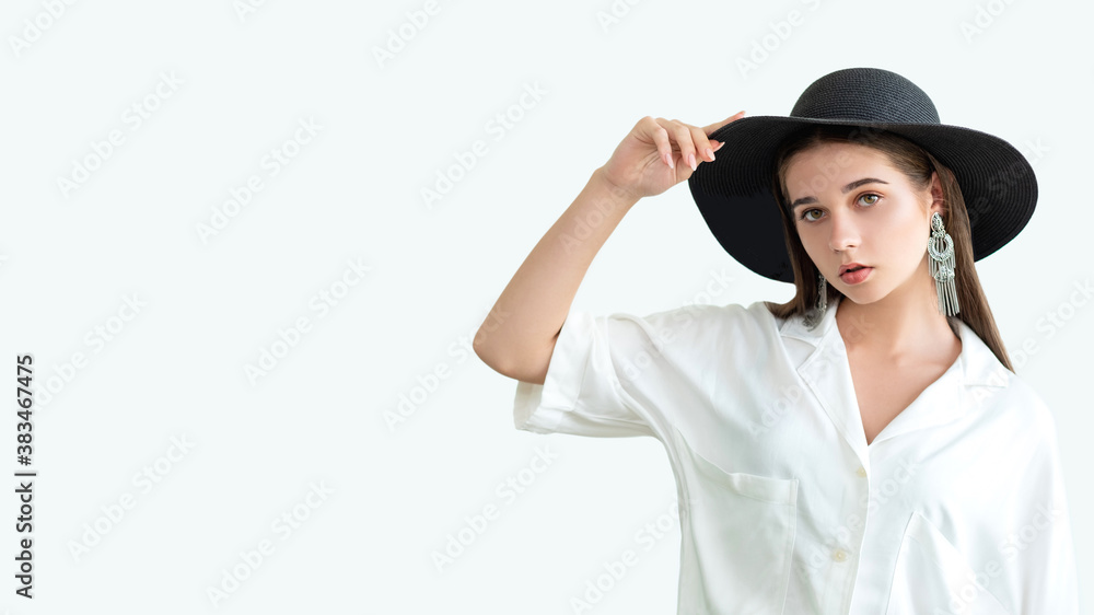 Boho trend. Summer outfit. Young glamorous woman in wide-brimmed black hat vintage earrings white blouse looking at camera isolated on neutral copy space. Fashion model shooting. Style mixing Boho trend. Summer outfit. Young glamorous woman in wide-brimmed black hat vintage earrings white blouse looking at camera isolated on neutral copy space. Fashion model shooting. Style mixing