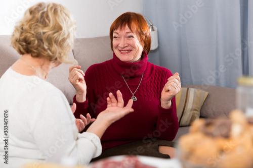 Smiling pensioners females talking on sofa in room at home