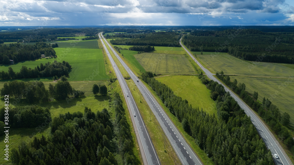 Aerial view of highway through fields and forests with cars. Cloudy day. Top view. Drone photo.

