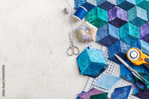 Fragment of tumbling blocks quilt, accessories for quilting on a white surface. Space for text.