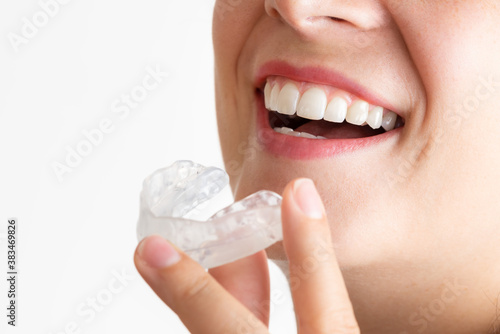 Close up on a young woman with beautiful smile while wearing a bruxism bite. Orthodontic appliance for dental correction on a perfect white teeth. Lady with clean mouth putting a mobile teeth aligner. photo
