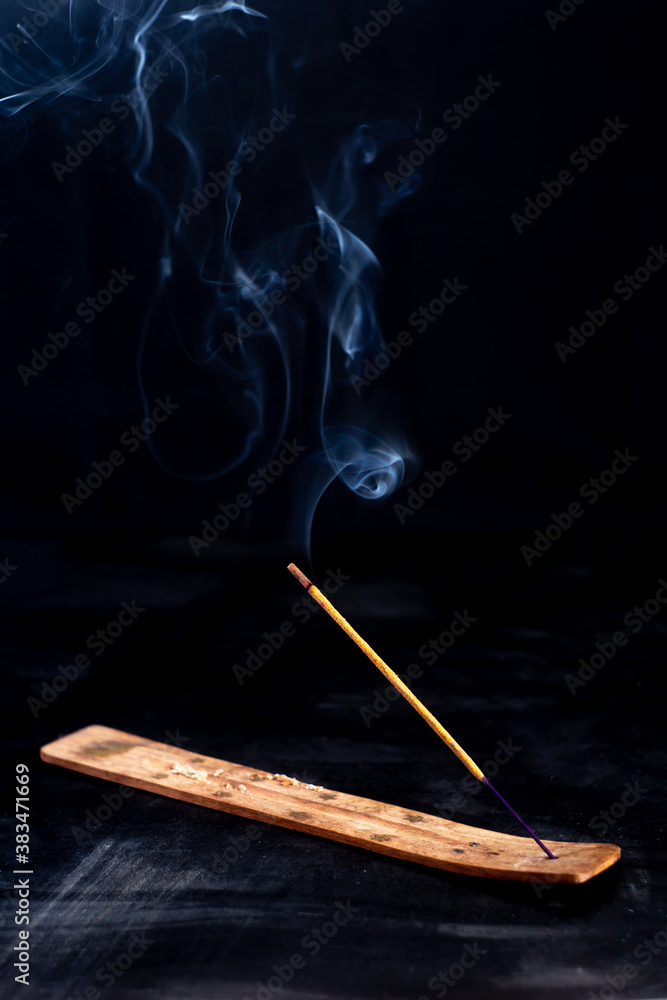 Incense stick with a wisp of smoke on a wooden stand. On a dark background Incense stick with a wisp of smoke on a wooden stand. On a dark background