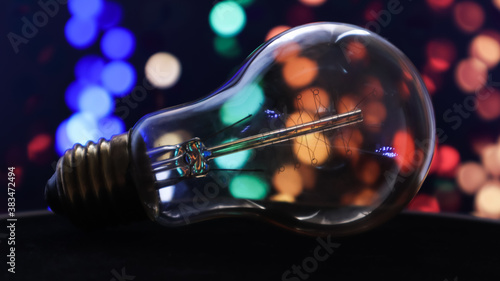 One light bulb lies on a black background with lights in the background. Creative ideas concept. Colorful background with flickering light bulbs. Holiday concept. New Year's and Christmas