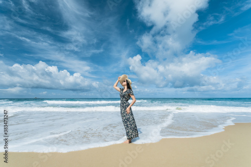 Quadro su tela Beautiful Asian women in a floral kaftan in a white brim hat stands on the beach