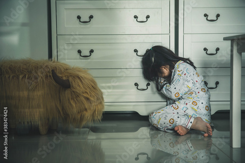 Sad little girl sitting on floor indoors. Child in danger. Sad little girl closing eyes with hands on floor indoors. Child inhuman concept. photo