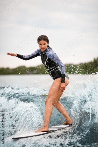 handsome woman stands on a surfboard and actively rides on the wave © fesenko