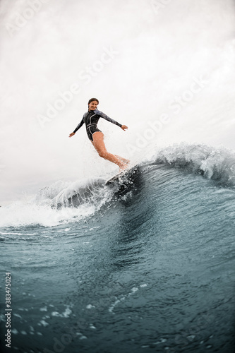 beautiful view on smiling woman who elegantly stands on the board and rides down the wave