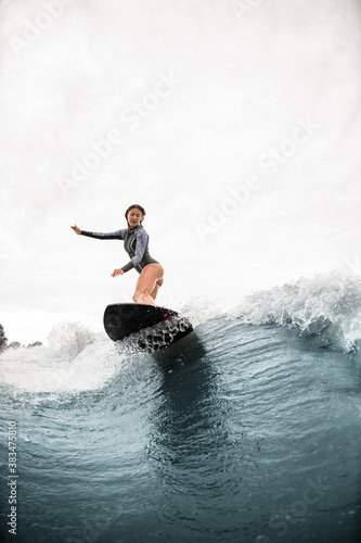 View on woman who stands on a surfboard and rides on the wave