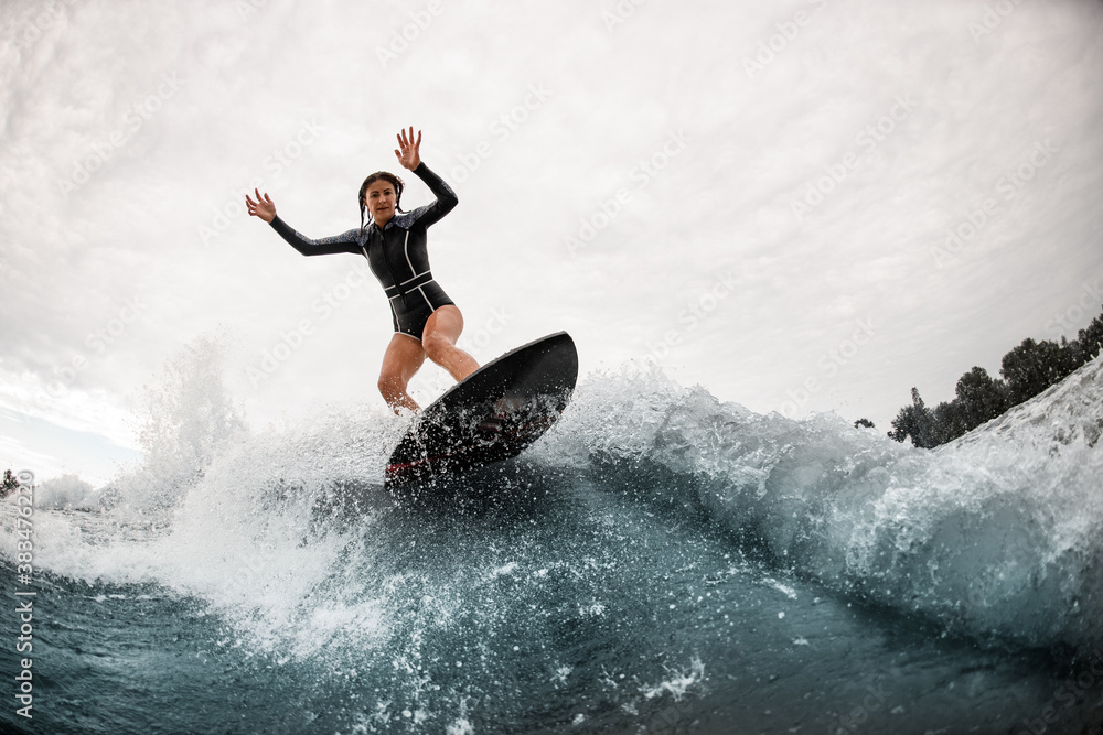 sporty woman stands on a surfboard and actively balances on the wave