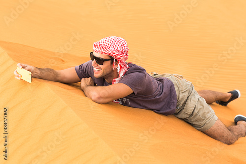 Photography Male tourist taking a selfie picture with his mobile phone while lying on the desert sand dune