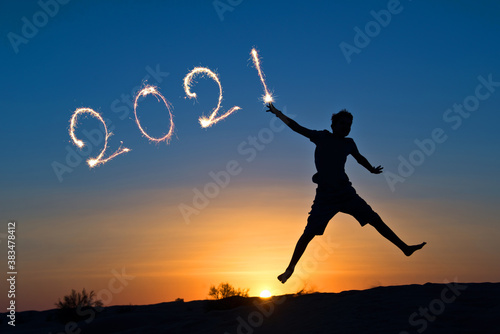 2021 written with sparkles, silhouette of a boy jumping in the sun, holiday card