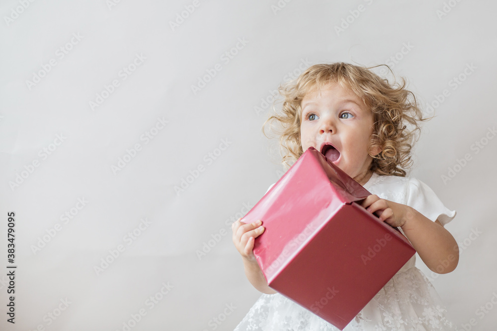 Excited curly girl in white dress with Christmas gift on light gray background Excited curly girl in white dress with Christmas gift on light gray background