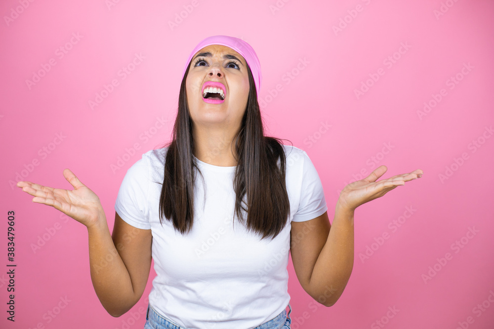 Young beautiful woman wearing pink headscarf over isolated pink background clueless and confused expression with arms and hands raised Young beautiful woman wearing pink headscarf over isolated pink background clueless and confused expression with arms and hands raised