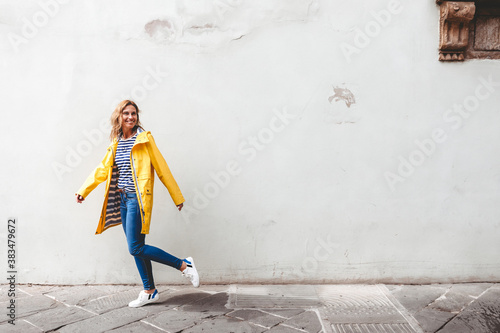happy woman walking on a street n front of a wall looking back 