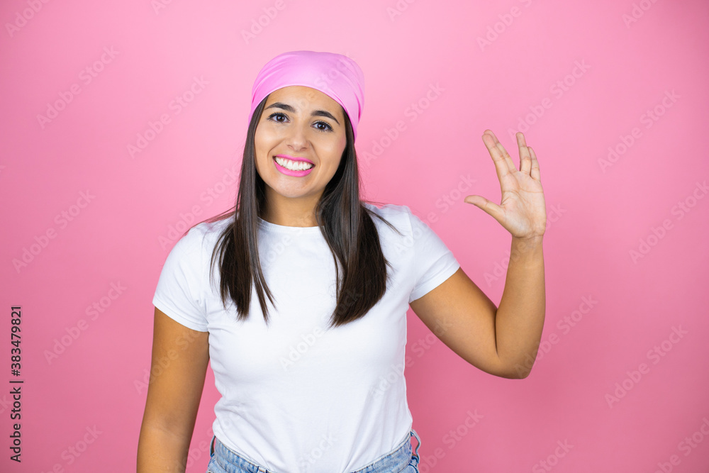 Young beautiful woman wearing pink headscarf over isolated pink background doing star trek freak symbol Young beautiful woman wearing pink headscarf over isolated pink background doing star trek freak symbol