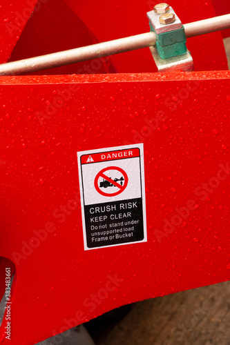 Danger warning sign of Crush Risk with symbol and Keep clear of frame or bucket on red forklift tractor. Norfolk, UK - October 4th 2020