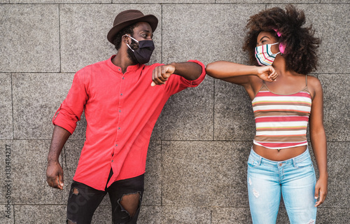 Happy black friends wearing protective masks while bumping their elbows instead of greeting with a hug - Social distance beetween people concept - Focus on faces photo