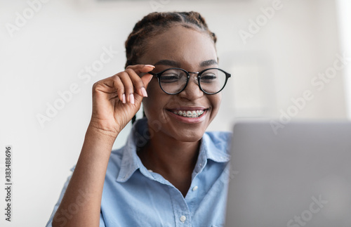 Young Specialist. African lady with eyeglasses and braces using laptop in office