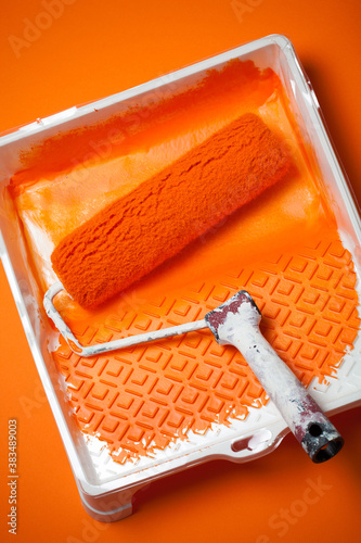 Orange paint roller in tray with orange paint on orange background