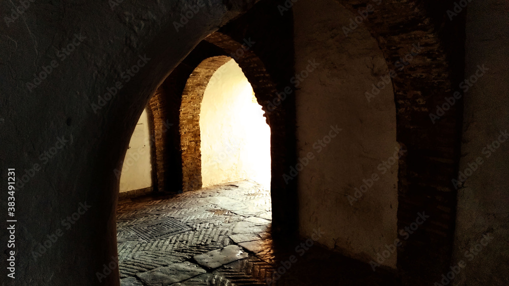 ancient medieval dark passage or corridor with arches in the old town of Seville, Spain, with light at the end of the tunnel