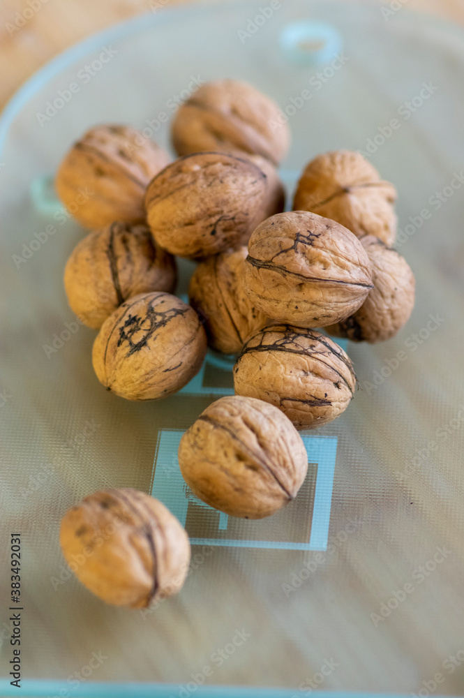 Walnuts on bamboo wooden table in hard shells, pile of dry ripened fruits on glass cutting board, harvested food ingredient