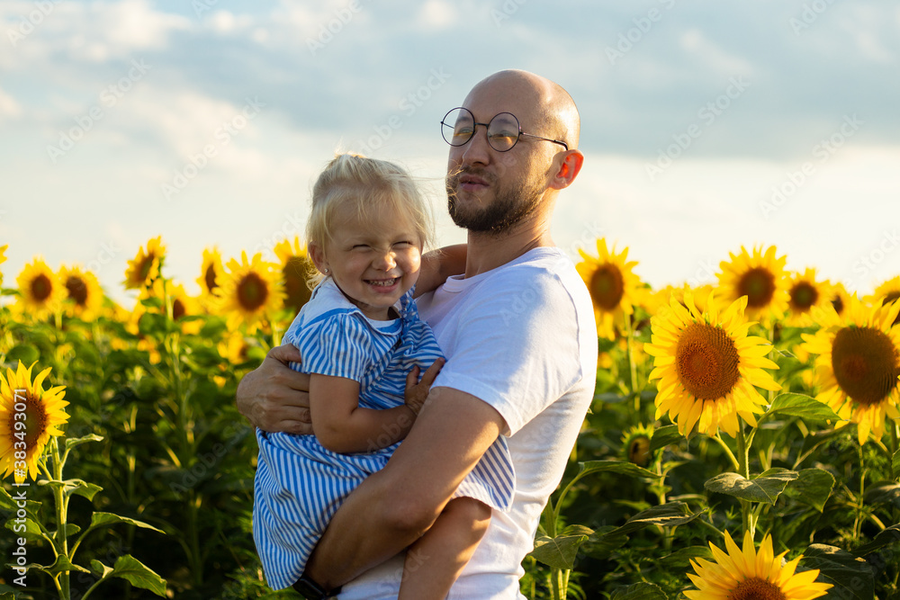 Young man holding a baby in his arms on a sunflower field Young man holding a baby in his arms on a sunflower field
