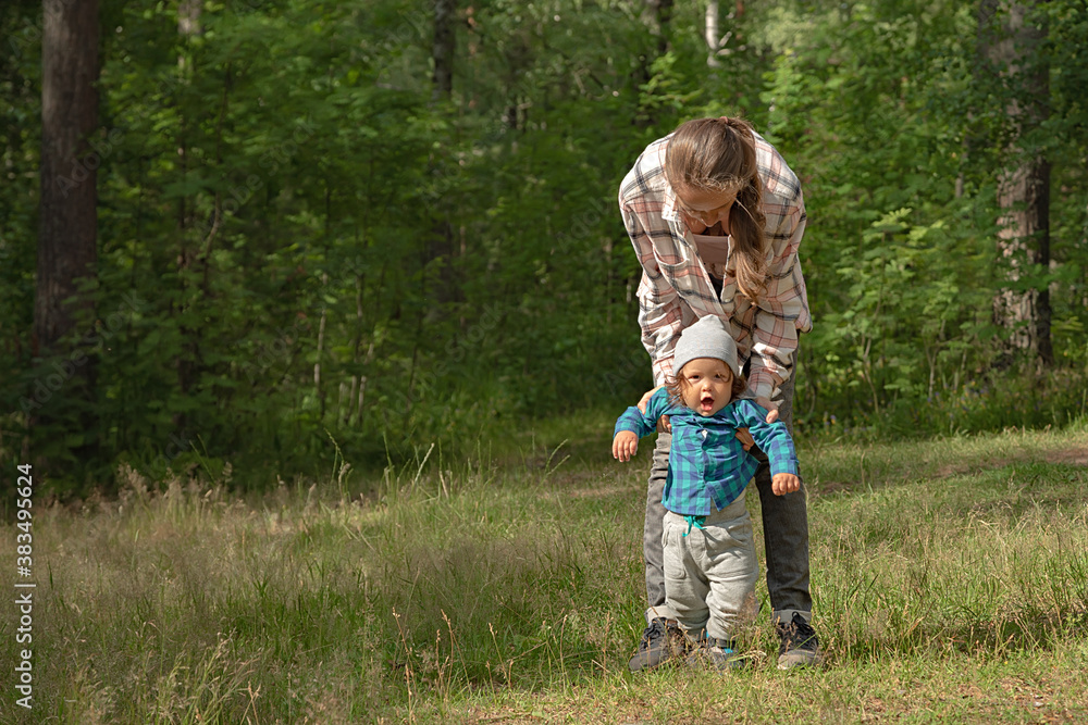 Adorable toddler taking the first steps and walking with the help of the mother on the background of the green forest. Adorable toddler taking the first steps and walking with the help of the mother on the background of the green forest.