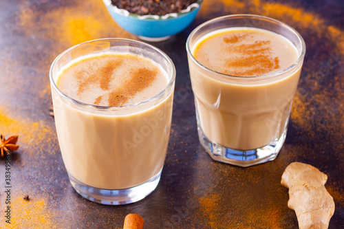 Masala chai tea on a black background. Two transparent glasses of masala tea and scattered various spices. Top view