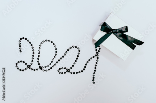 White gift or present box with black ribbon and 2021 number made of beads on white background. Flat lay composition for birthday, Christmas, wedding. Free copy space for text.