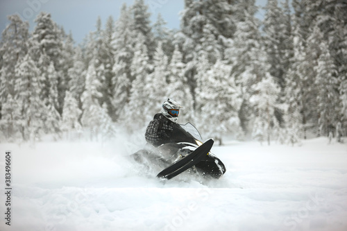 Snowmobile rider racing and jumping at high speed in outfit and helmet against the background of snow and forest.