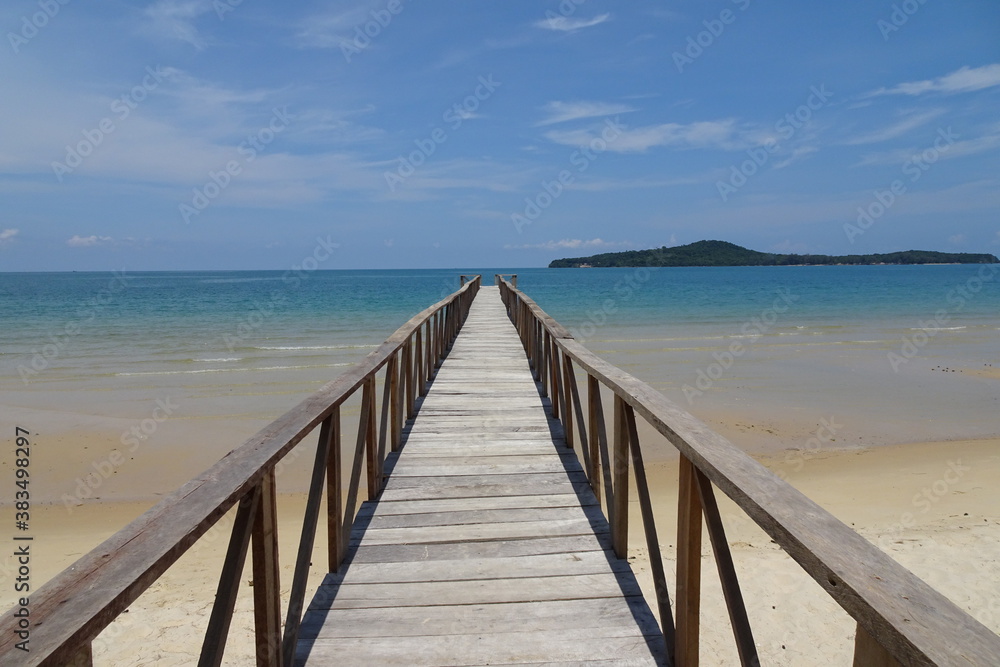 Wooden bridge leading into the ocean across a beach towards an island from Koh Ta Kiev Cambodia
