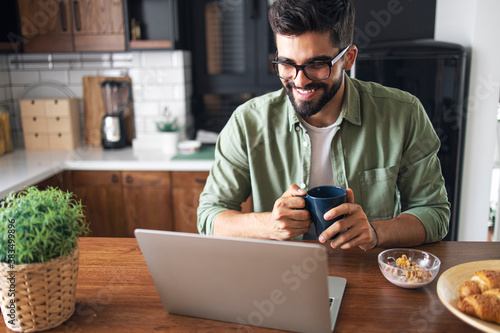 Guy holding coffee mug, looking at laptop, smiling