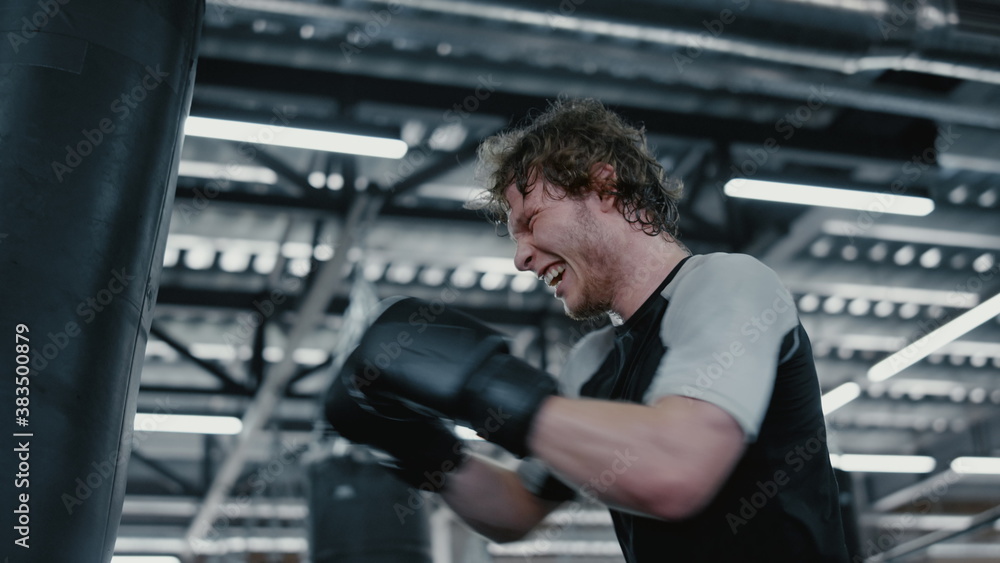Anxious fighter hitting punching bag at gym. Kickboxer working on blows Anxious fighter hitting punching bag at gym. Kickboxer working on blows