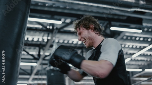 Anxious fighter hitting punching bag at gym. Kickboxer working on blows