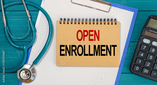 Notepad with text OPEN ENROLLMENT, calculator and stethoscope.