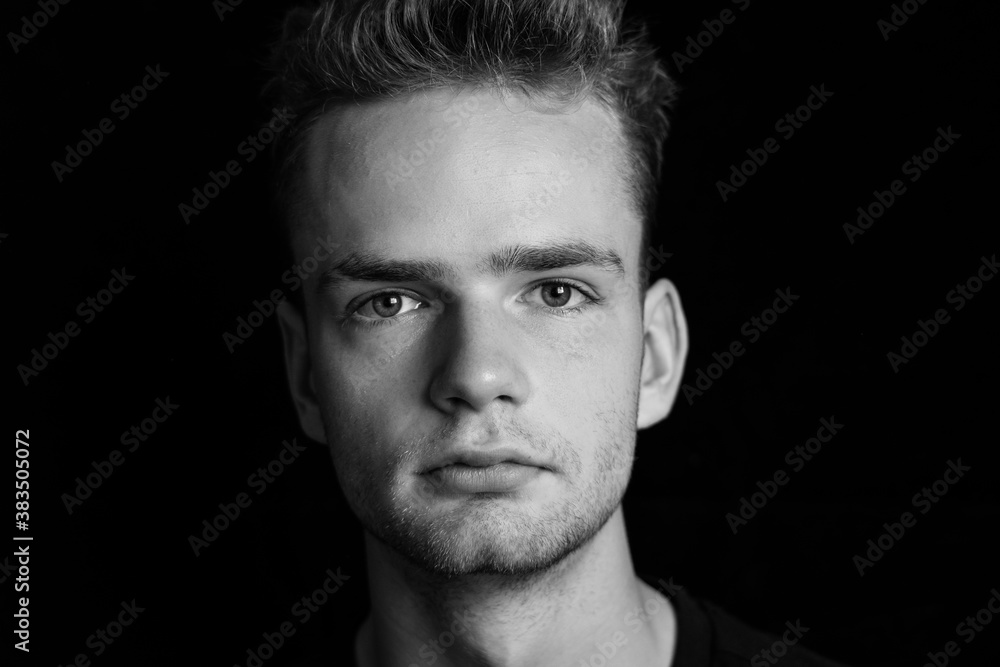 Portrait of a serious young guy on a dark background, black and white photo