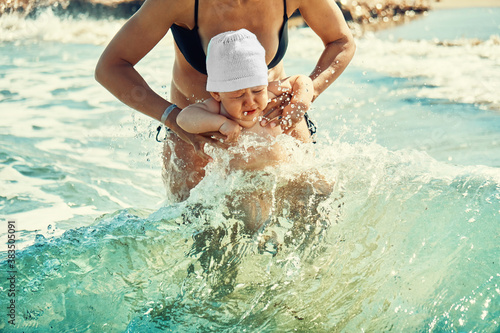 Crop mother dipping baby in sea water