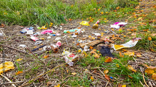 Heap of rubbish on grass in the autumn park. Plastic and glass bottles, bottle caps and paper. Concept of environmental protection and littering of environment.